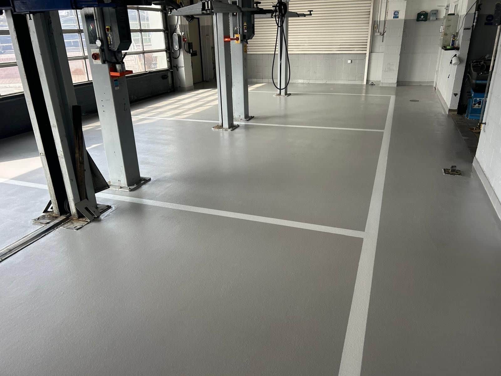 Light grey Monargrip resin flooring with vehicle bay markings and yellow hazard chevrons in a Mansfield automotive workshop.